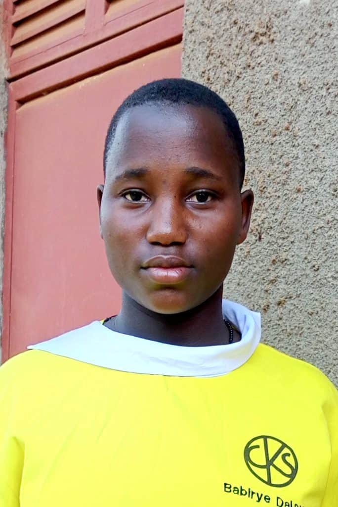 Young student in yellow sports jersey standing outdoors, representing empowerment through education sponsorship for vulnerable children.