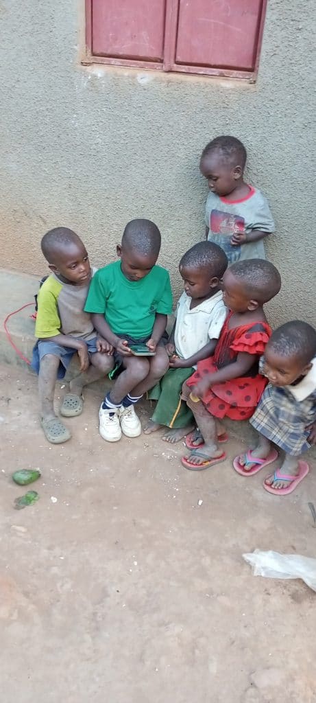 Children sitting outdoors, using a tablet device, highlighting the role of technology in education for underserved communities.