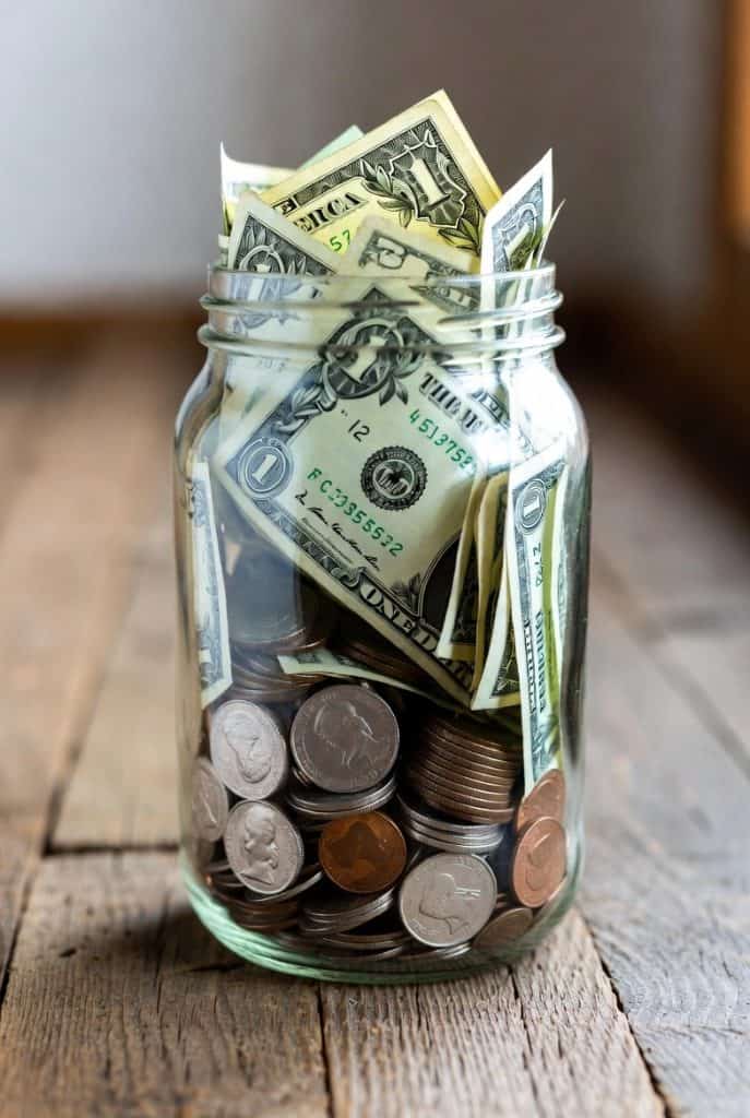 Glass jar filled with dollar bills and coins, symbolizing donations to support students' education through Pearl Global Ministries.