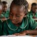 Young students in green uniforms engaged in learning activities in a classroom setting, highlighting education and community development.